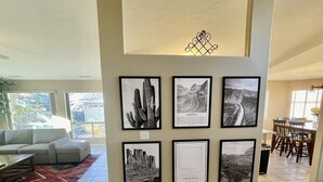 A living room with a large wall-mounted art display, a patterned rug, and a dining area in the background. - Spacious Pet-Friendly Home w/Fenced Yard & Central (Prescott)