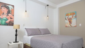 Quarto com uma cama, mesa de cabeceira, luminária e duas obras de arte na parede.