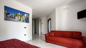 A modern hotel room with a red sofa, a bed with a red duvet, and a large painting of a coastal village. - Agriturismo Liscio by Rentbeat (Noci)