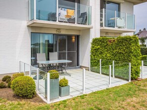 A modern two-story residential building with a balcony, a glass door entrance, and a small patio area with a table and chairs. - Apartment With Spacious Terrace (Middelkerke)