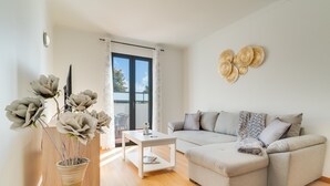 Un salon moderne avec un canapé d’angle gris, une table basse blanche et un vase contenant des fleurs artificielles.