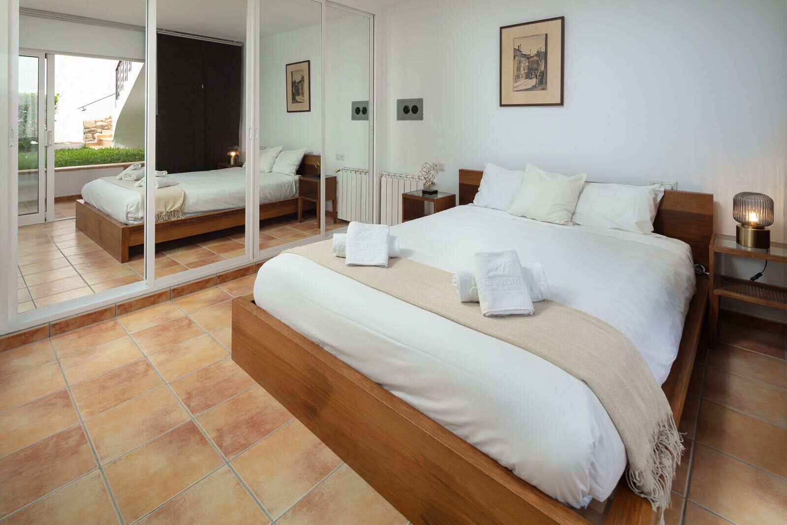 A spacious bedroom with a large bed, a mirrored closet, and a view of the outdoors.