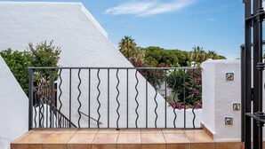 A white building with a metal staircase and railing, surrounded by greenery and flowers.