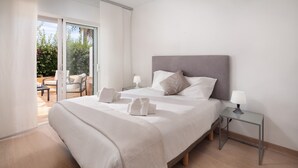 A modern bedroom with a large bed, two bedside tables, and a sliding glass door leading to an outdoor patio.