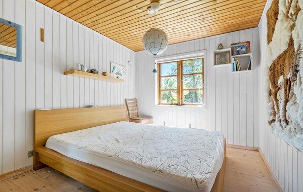 A bedroom with a wooden bed, a window with a view, a shelf with books, and a wall-mounted heater.