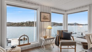 A room with large windows overlooking a lake, a framed picture on the wall, and a lamp on a small table.