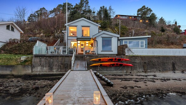 A coastal house with a dock leading to a beach, kayaks, and a well-lit entrance.