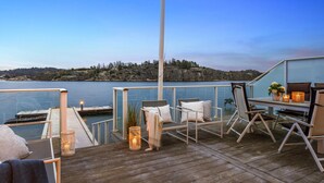 A deck with outdoor seating, a table with candles, and a view of a calm lake and rocky shoreline at dusk.