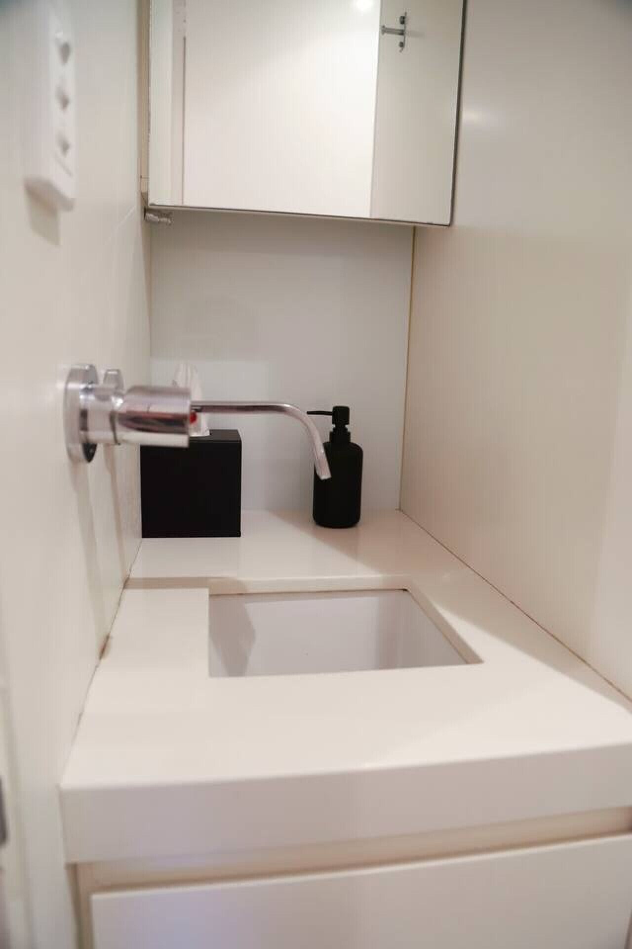 Een kleine badkamer met een wit wastafel, een zwarte zeepdispenser en een wit kastje erboven.