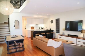 Een modern appartement met een eethoek, bank, televisie, keuken en een trap.