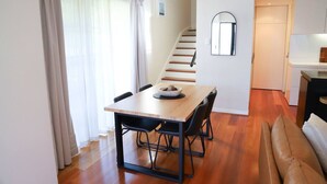 Un interior modern amb una taula de menjador, cadires, una escala i una zona de cuina.