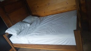 Een houten bed met witte lakens in een kamer met houten wanden en een donkere vloer.
