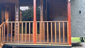 Een houten terras met een leuning, een overdekte veranda en een stenen muur op de achtergrond.