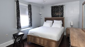 A bedroom with a wooden bed, a small stool, a desk, a ceiling fan, and a window with curtains. - Serene modern 3-bedroom house in Shillington (Shillington)