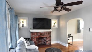 A living room with a fireplace, a television, and a ceiling fan. - Serene modern 3-bedroom house in Shillington (Shillington)
