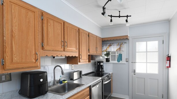 A kitchen with wooden cabinets, a stainless steel sink, a coffee maker, a toaster, and a dishwasher. - Serene modern 3-bedroom house in Shillington (Shillington)