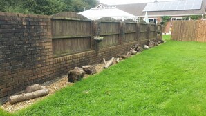A brick wall with a wooden fence, a grassy area, and a solar panel house in the background. - Peaceful Secluded One Bedroom Chalet – Sleeps 4, Large Garden, Pets Welcome (Tondu)