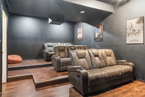 Une salle de cinéma maison équipée de trois canapés en cuir inclinables, d’un escalier en bois et de posters encadrés accrochés au mur.