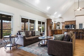 A spacious living area with a large sofa, a coffee table, and a view of a forest through large windows.