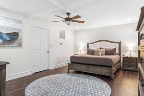 Quarto com cama, ventoinha no teto, tapete redondo e cômoda.