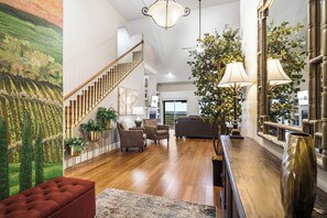 Ein geräumiges Wohnzimmer mit einer Holztreppe, einem großen Gemälde und mehreren Sitzbereichen.