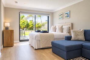 A bedroom with a bed, a blue sofa, a wooden cabinet, and a view of the outdoors. - High Tides Elegant 5-Bed Villa & Hot Tub Sandbanks (Sandbanks)