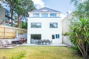 Ett modernt hus i två våningar med en uteplats, utemöbler och en liten trädgård.