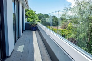 Un balcon doté d’un plancher en bois, d’une plante en pot et d’une rambarde en verre donnant sur un espace verdoyant.