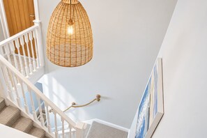 A staircase with white balusters, a wicker pendant light, and a framed picture on the wall.