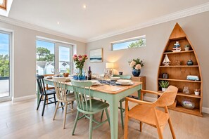 A dining area with a wooden table and chairs, a vase with flowers, and a bookshelf with various items. - High Tides Elegant 5-Bed Villa & Hot Tub Sandbanks (Sandbanks)