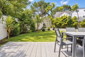 A wooden deck with a table and chairs, surrounded by a well-maintained lawn and various trees. - High Tides Elegant 5-Bed Villa & Hot Tub Sandbanks (Sandbanks)