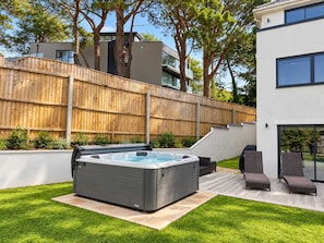 Un espace moderne aménagé à l’extérieur avec un jacuzzi, une clôture en bois, une pelouse et une terrasse dotée de chaises longues.