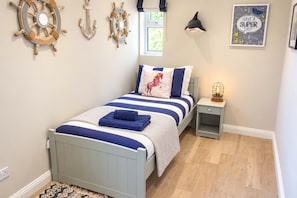 Une chambre à coucher comprenant un lit, une table de chevet, une lampe fixée au mur et des éléments de décoration murale sur le thème de la marine.