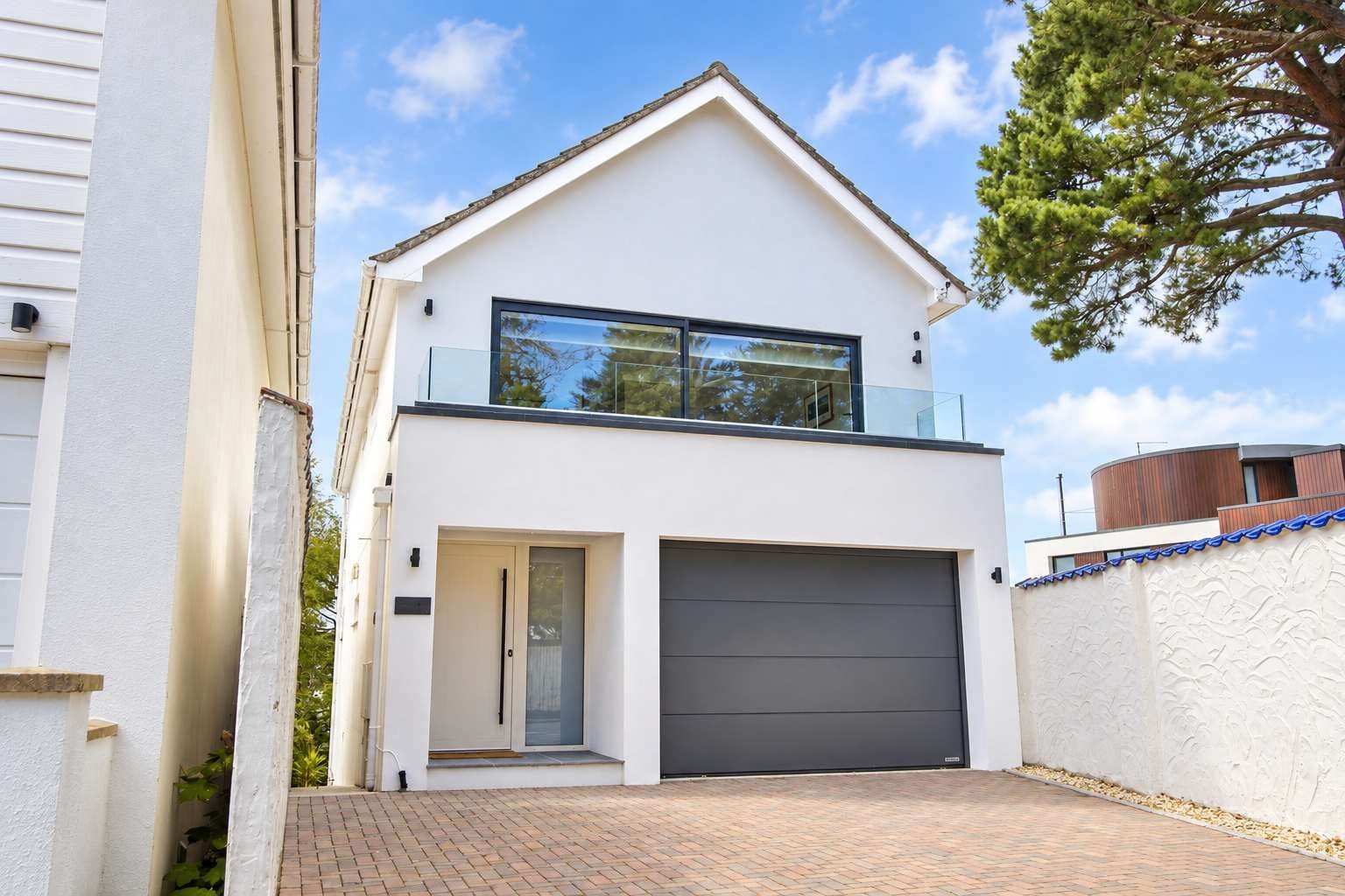 Une maison moderne à deux étages, dotée d’un garage, d’un balcon et d’une allée pavée en briques.