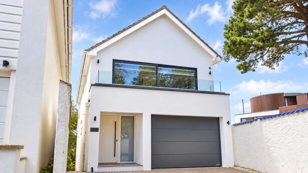 Et moderne hus med to etager, garage, balkon og en indkørsel med brosten.