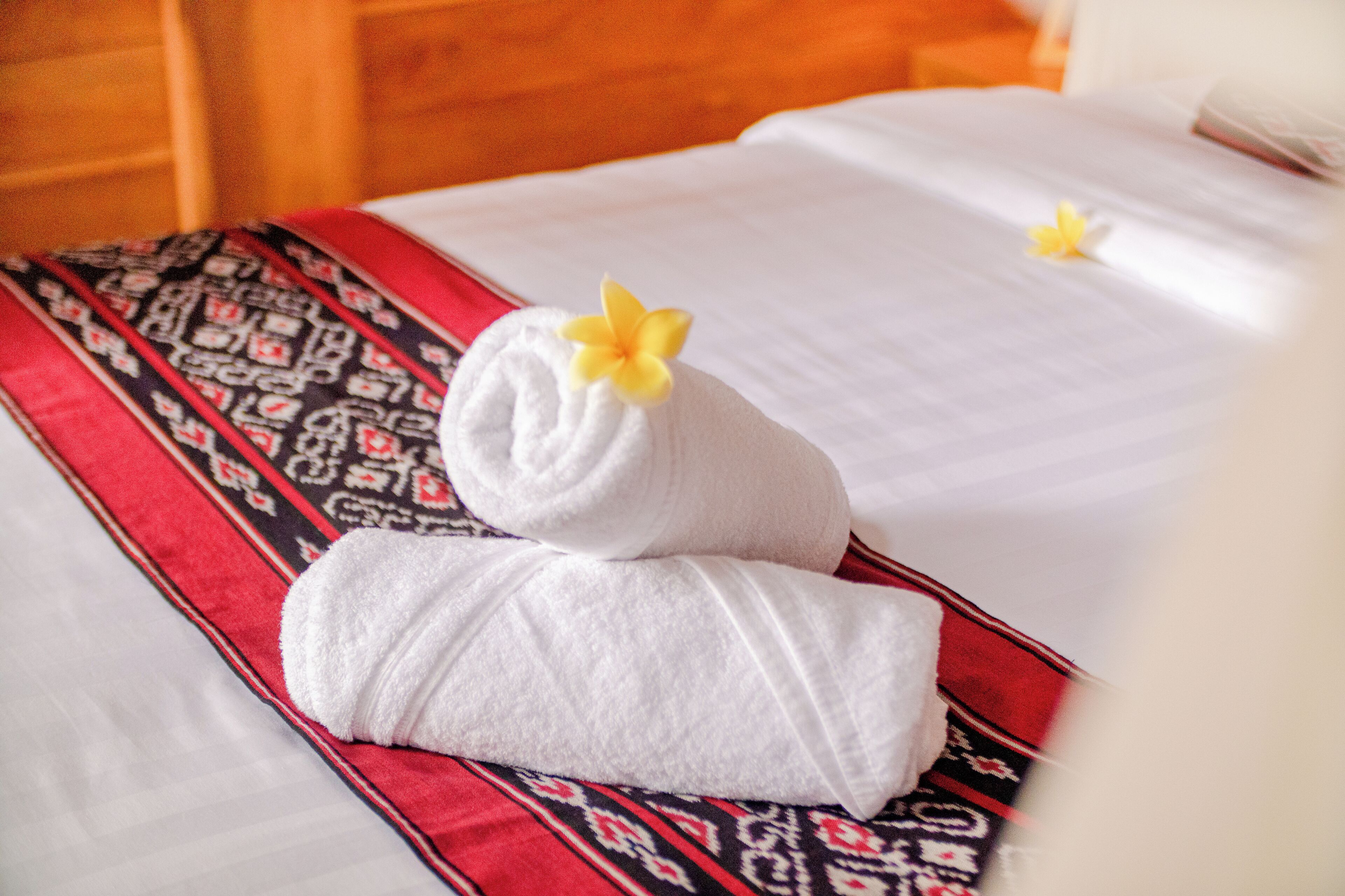 Un lit bien fait, recouvert d’une couvre-lit à motifs, avec deux serviettes ornées de fleurs jaunes.