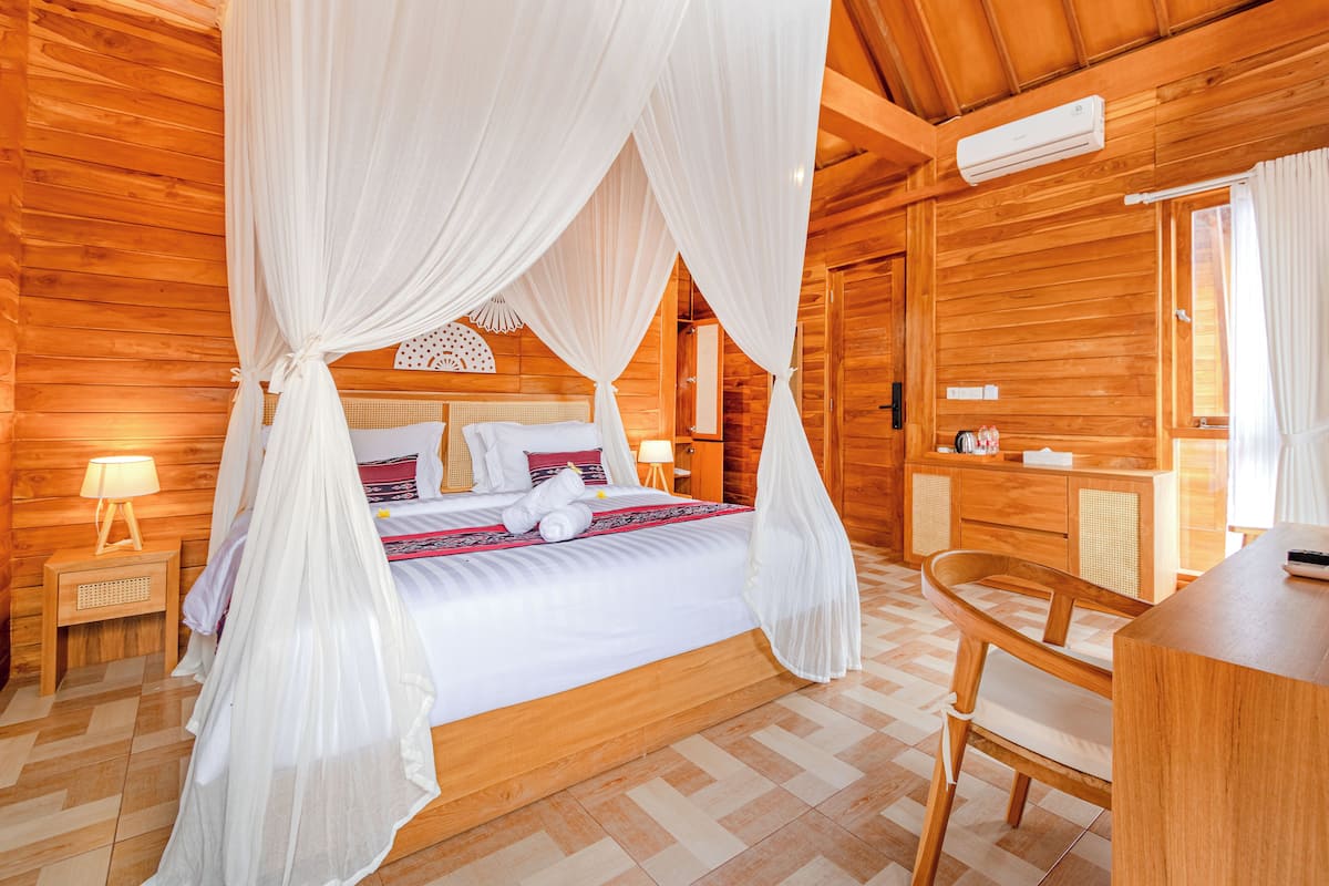 A wooden cabin bedroom with a four-poster bed, a bedside table with a lamp, and a wooden chair.