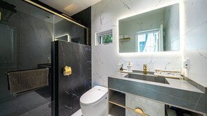 A modern bathroom with a marble shower enclosure, a toilet, and a vanity with a large mirror. - EUDAIMONIA (Jeju City)