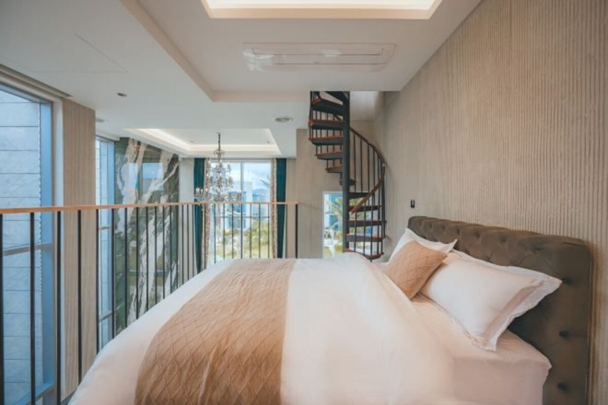 A bedroom with a large bed, a spiral staircase, and a view of the outdoors.