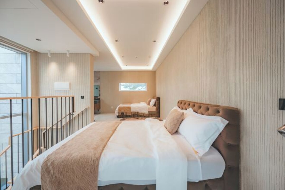 A modern hotel room with a large bed, a small desk, and a balcony with a railing.