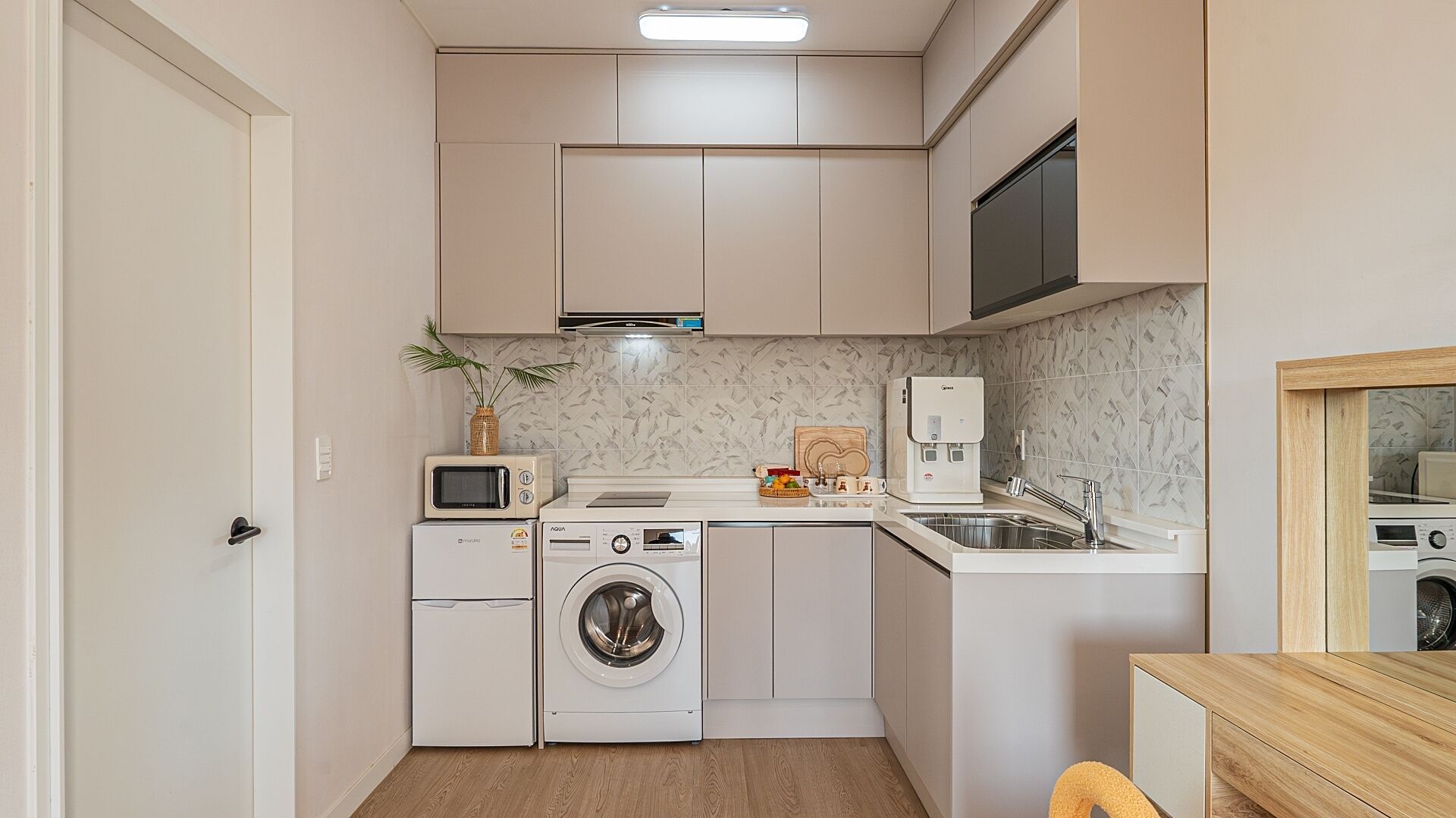 Una cocina compacta equipada con lavadora, microondas y dispensador de agua.