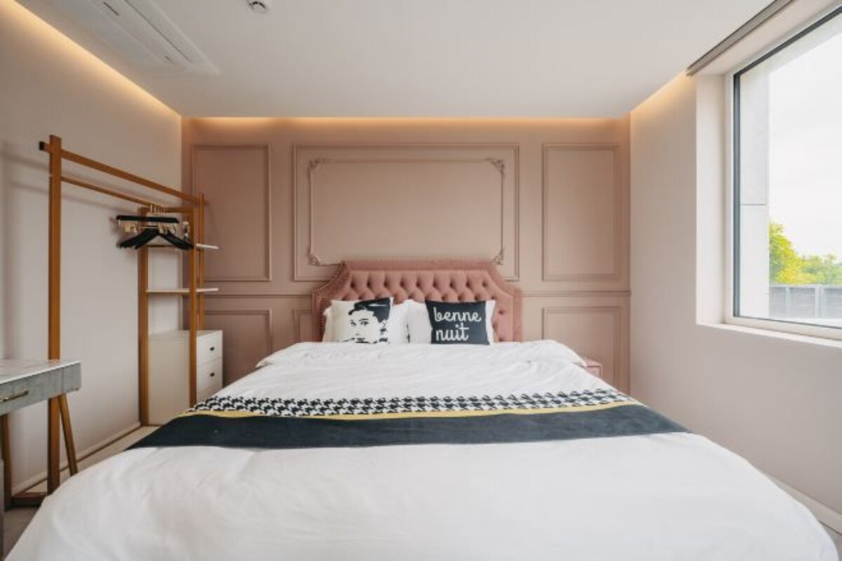 A bedroom with a bed, a bedside table, a hanging rack, and a window.