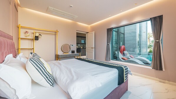 A modern bedroom with a large bed, a vanity, a walk-in closet, and a balcony with a pool view. - EUDAIMONIA (Jeju City)