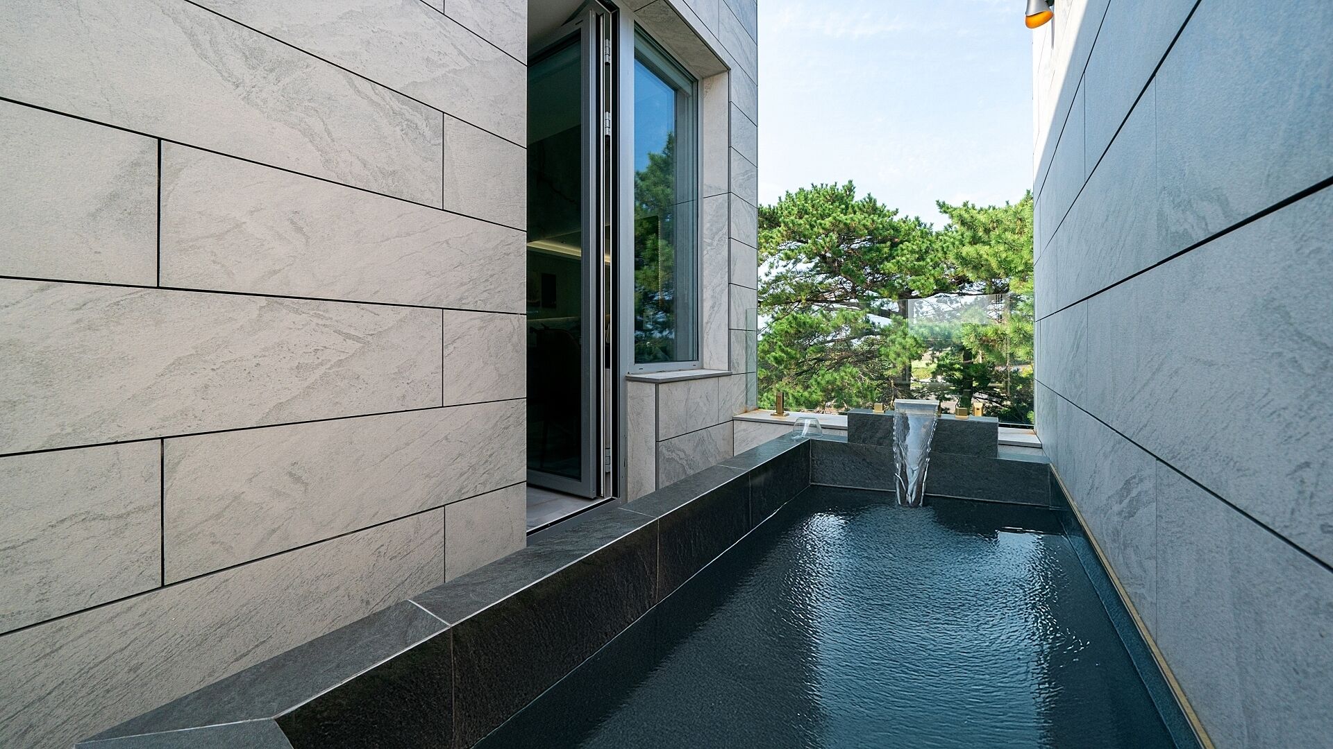Un edificio moderno con una fuente de agua estrecha y una puerta de cristal.