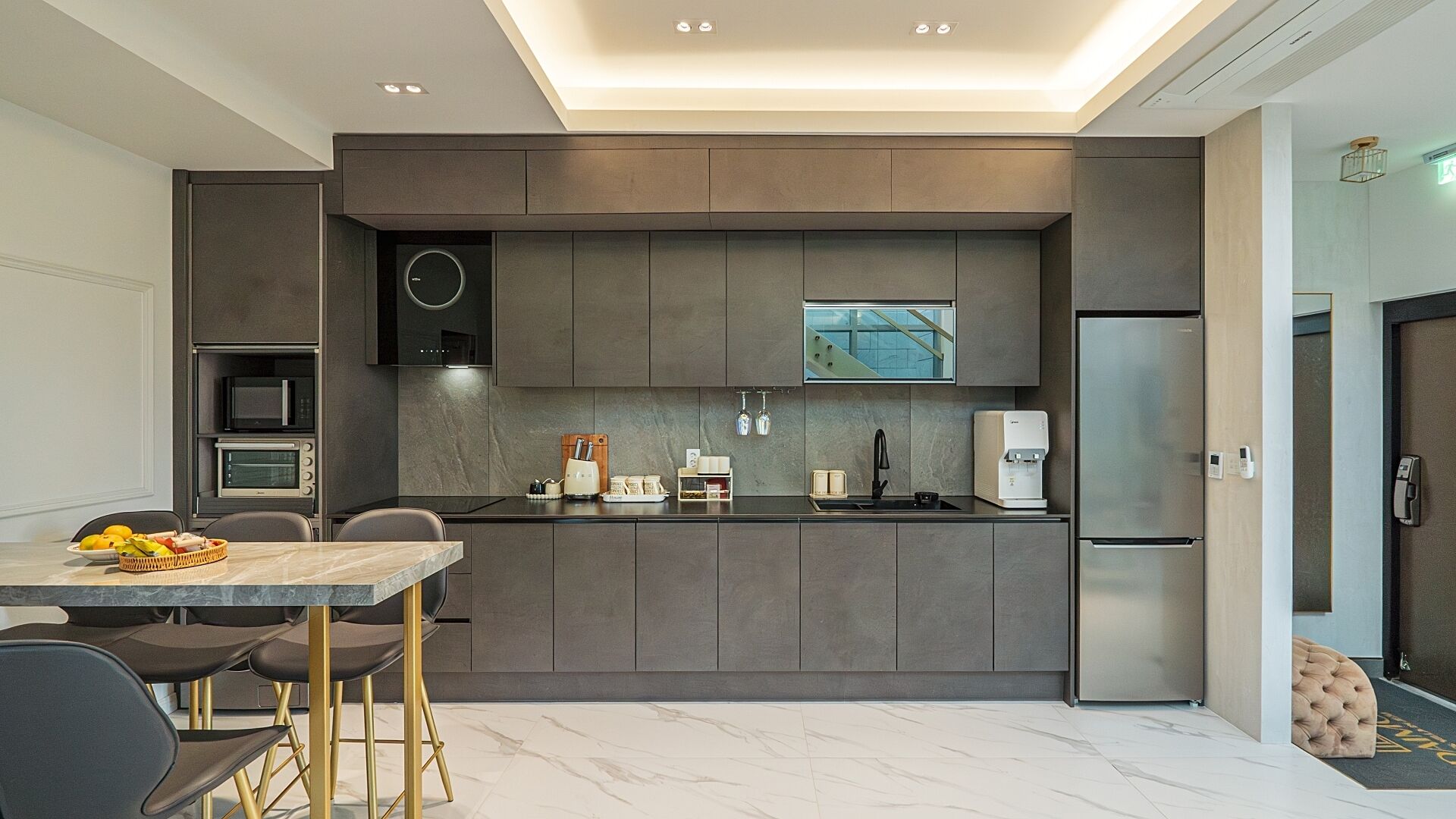 Una cocina moderna con armarios grises, microondas integrado y refrigerador de acero inoxidable.