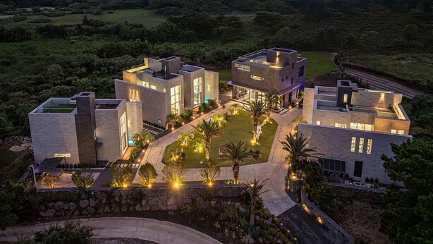 A modern, multi-story building with a landscaped garden, featuring a swimming pool and outdoor seating areas. - EUDAIMONIA (Jeju City)