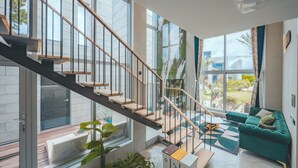 A modern interior with a staircase, a green sofa, and large windows. - EUDAIMONIA (Jeju City)