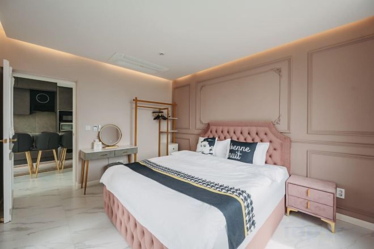 A bedroom with a large bed, bedside tables, a dresser, and a vanity with a mirror.