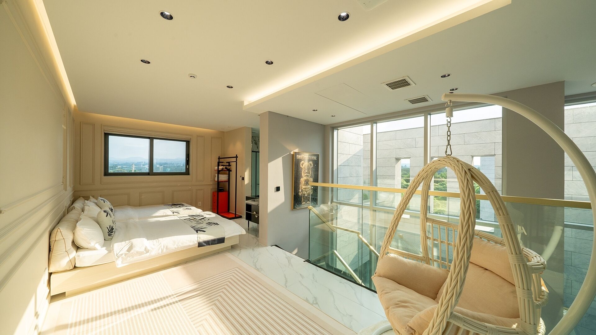 A modern hotel room with a large bed, a hanging chair, and a view of the city through large windows.