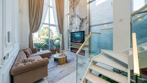 A modern living room with a large sofa, a coffee table, and a fireplace. There is a TV mounted on the wall and a staircase leading to an upper level. - EUDAIMONIA (Jeju City)